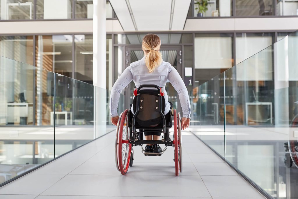 Woman in wheelchair moving across a glass walled hallway